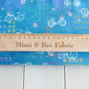 White bicycles with pretty baskets and flowers on a mid blue cotton fabric by Robert Kaufman